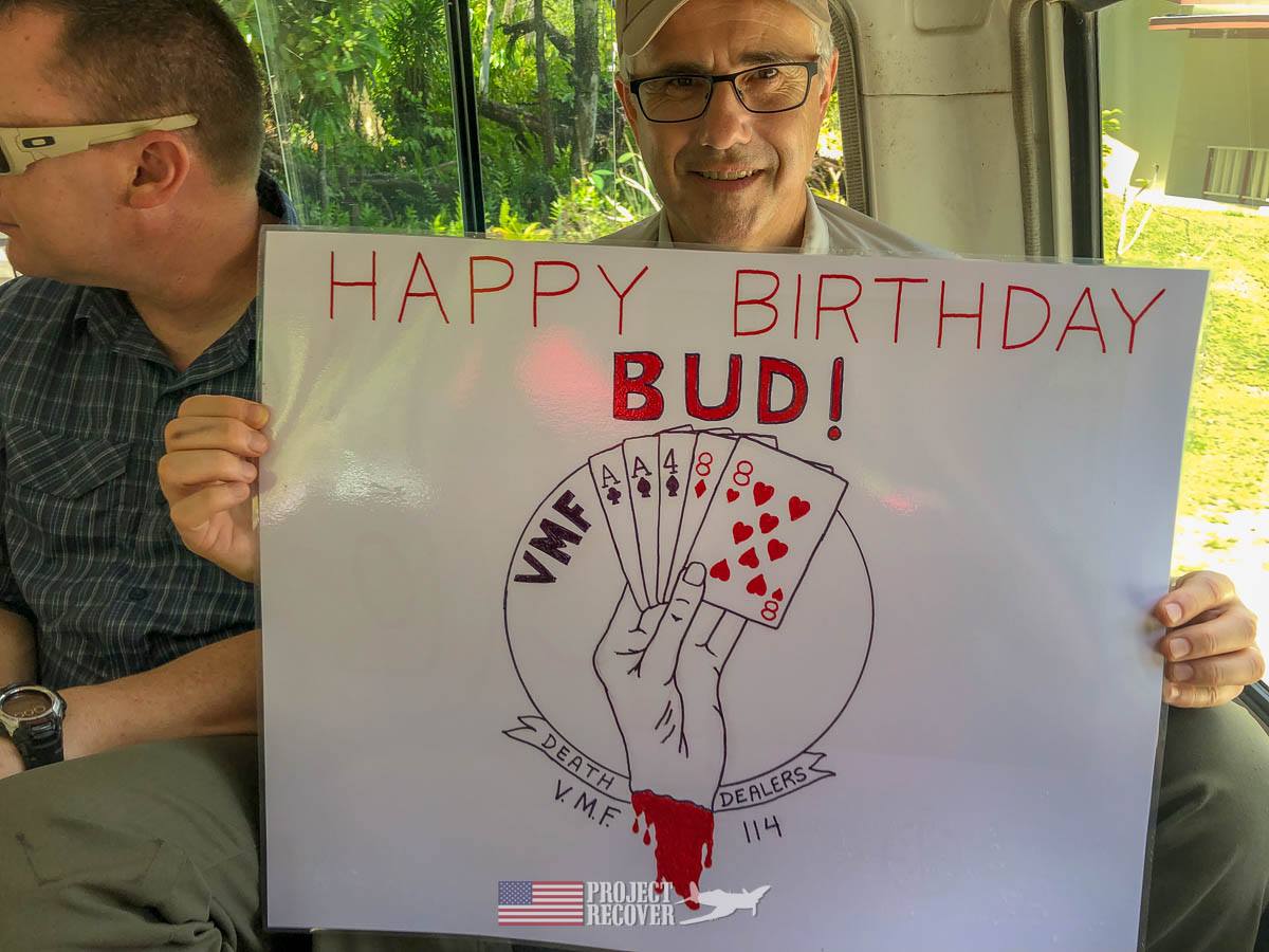 Glenn Frano holds sign wishing Happy Birthday to Glenn ‘Bud’ Daniel, WWII Corsair pilot who flew during Battle of Peleliu.